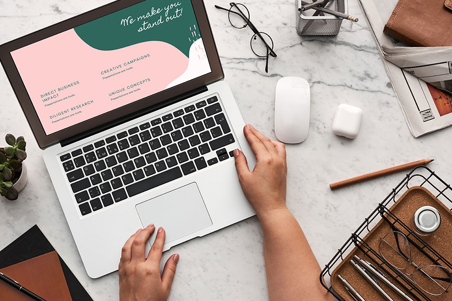 Creative Campaign Planning Desk Person working on laptop with design concepts, surrounded by office items on a marble desk.