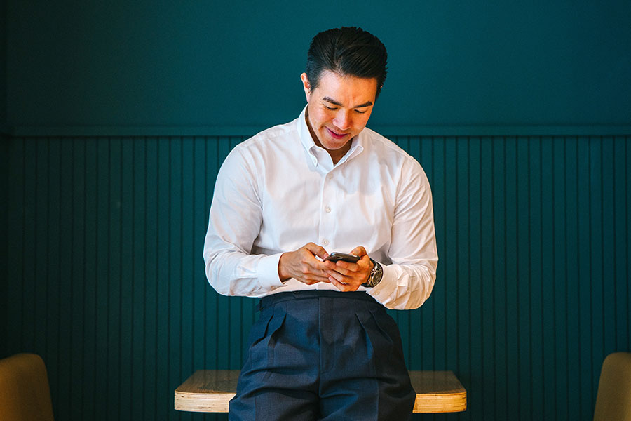 Smartphone Joy Indoors Person in white shirt and dark pants smiles at smartphone indoors against dark wall and wood surface.